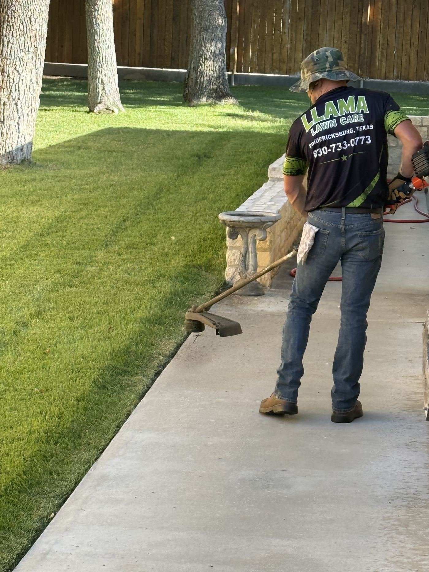 Llama Lawn Care crew member trimming in a branded shirt